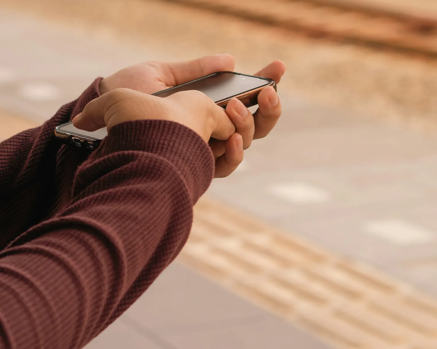 Mãos segurando o celular na plataforma de uma estação