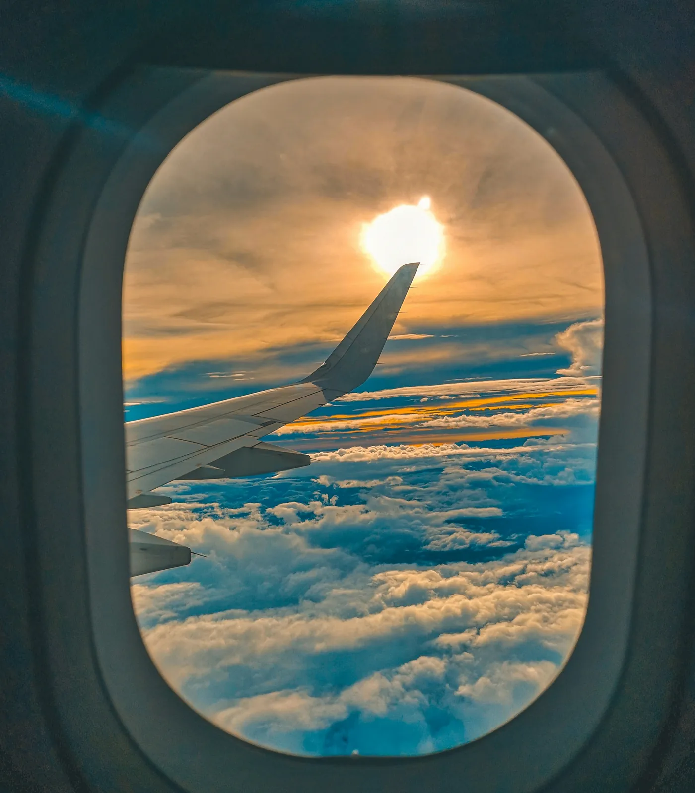 Asa do avião e o sol sobre as nuvens, vistos pela janela
